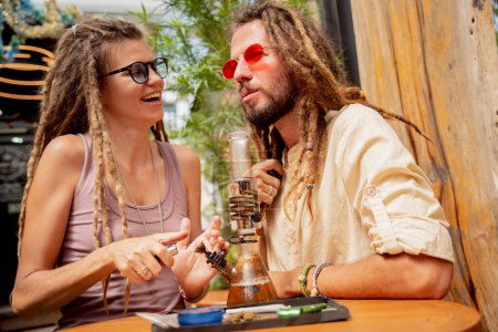 Téléchargez les photos : Hippie style couple smoking medical marijuana using a bong. - en image libre de droit