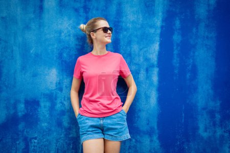Foto de Modelo femenino con camiseta en blanco rosa en el fondo de una pared azul - Imagen libre de derechos