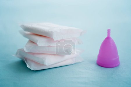 Foto de Menstrual cup and pads on a blue background, concept of critical days. - Imagen libre de derechos
