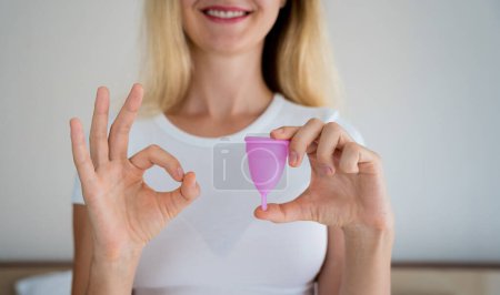Foto de Joven hermosa mujer en casa sosteniendo una copa menstrual en sus manos. - Imagen libre de derechos