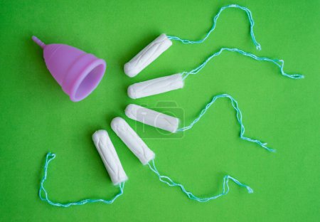 Téléchargez les photos : Menstrual cup, tampons on a green background, concept of critical days. - en image libre de droit