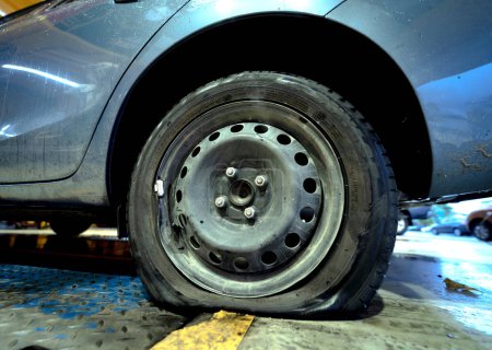 Foto de Car with a punctured and broken wheel in a car repair shop. - Imagen libre de derechos