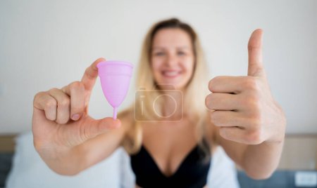 Photo for Young beautiful woman at home holding a menstrual cup in her hands. - Royalty Free Image