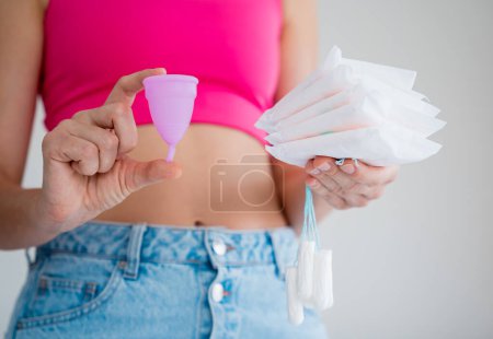 Téléchargez les photos : Jeune femme tenant la coupe menstruelle, tampons et serviettes hygiéniques dans ses mains. - en image libre de droit