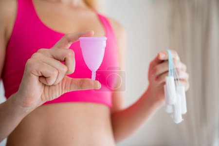 Téléchargez les photos : Jeune femme tenant à ses mains coupe menstruelle et tampons. - en image libre de droit