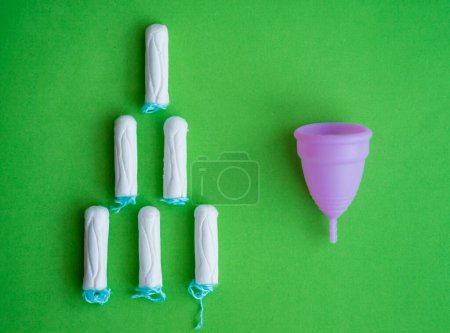 Foto de Copa menstrual, tampones sobre fondo verde, concepto de días críticos. - Imagen libre de derechos