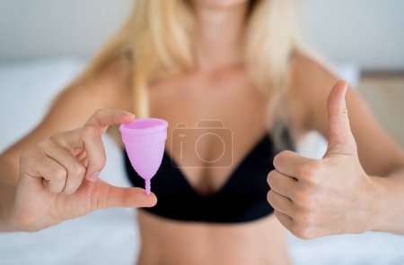 Photo for Young beautiful woman at home holding a menstrual cup in her hands. - Royalty Free Image