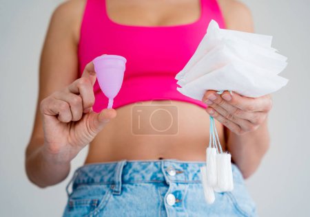 Foto de Mujer joven sosteniendo la copa menstrual, tampones y toallas sanitarias en sus manos. - Imagen libre de derechos