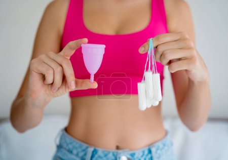 Foto de Young woman holding at her hands menstrual cup and tampons. - Imagen libre de derechos