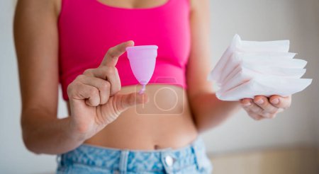 Foto de Mujer joven sosteniendo la copa menstrual y toallas sanitarias en sus manos. - Imagen libre de derechos