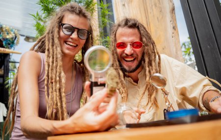 Téléchargez les photos : Hippie couple de style examine sous une loupe les articulations et les bourgeons de marijuana médicale. - en image libre de droit