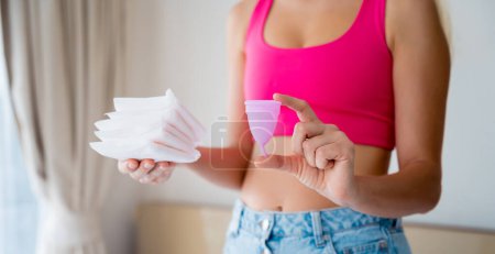 Téléchargez les photos : Jeune femme tenant une coupe menstruelle et des serviettes hygiéniques dans ses mains. - en image libre de droit