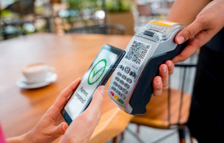 Mujer usando el pago sin contacto por teléfono móvil con código QR en la cafetería.