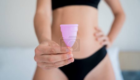 Foto de Young beautiful woman at home holding a menstrual cup in her hands. - Imagen libre de derechos