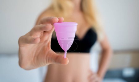Foto de Young beautiful woman at home holding a menstrual cup in her hands. - Imagen libre de derechos