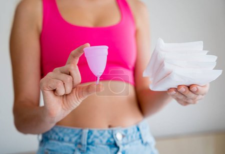 Téléchargez les photos : Young woman holding menstrual cup and sanitary pads in her hands. - en image libre de droit