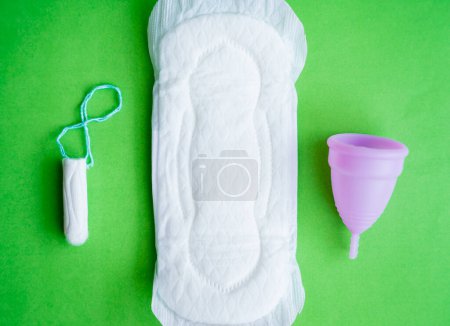 Foto de Almohadillas, copa menstrual, tampones sobre un fondo verde, concepto de días críticos. - Imagen libre de derechos