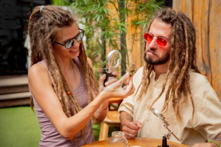 Photo for Hippie style couple examines under a magnifying glass the joints and buds of medical marijuana. - Royalty Free Image