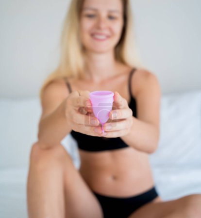 Téléchargez les photos : Young beautiful woman at home holding a menstrual cup in her hands. - en image libre de droit