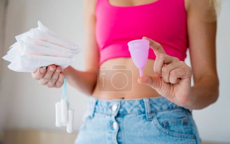 Téléchargez les photos : Young woman holding menstrual cup, tampons and sanitary pads in her hands. - en image libre de droit