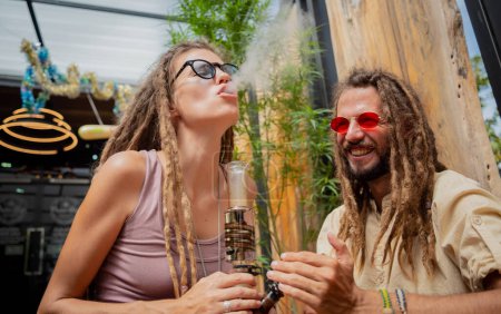Téléchargez les photos : Hippie style couple smoking medical marijuana using a bong. - en image libre de droit