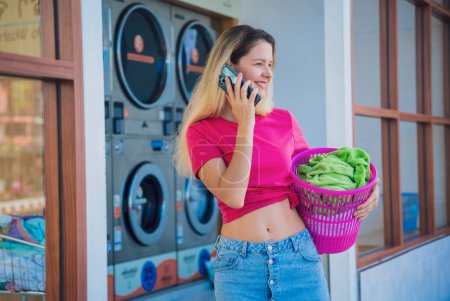Photo for Young beautiful woman talking by the phone in the laundry. - Royalty Free Image