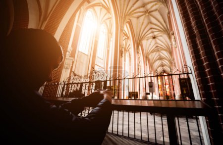 Téléchargez les photos : Silhouette de jeune homme priant à l'église au soleil. - en image libre de droit