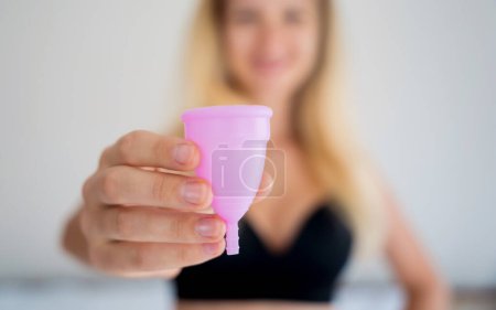 Foto de Joven hermosa mujer en casa sosteniendo una copa menstrual en sus manos. - Imagen libre de derechos