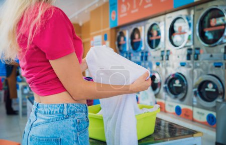Photo for Young beautiful woman washes and dries clothes in the laundry. - Royalty Free Image