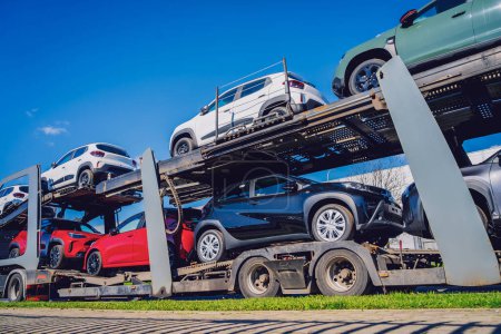 Car carrier trailer transports cars on highway at blue sky background