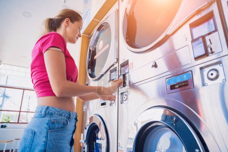 Foto de Mujer joven poniendo moneda en la lavadora en la lavandería. - Imagen libre de derechos