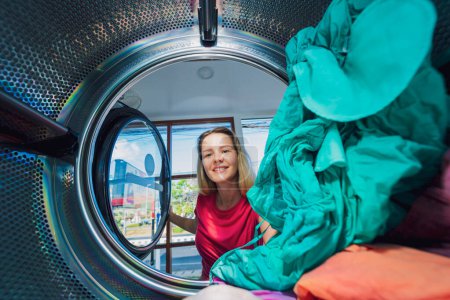 Téléchargez les photos : Jeune belle femme lave et sèche les vêtements dans la buanderie. - en image libre de droit