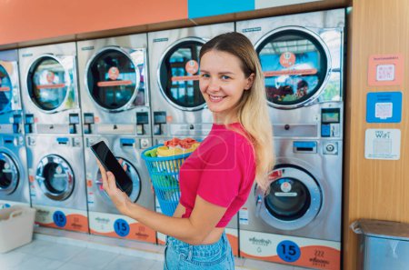 Photo for Young woman pays for laundry service using phone and banking application. - Royalty Free Image