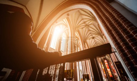 Téléchargez les photos : Silhouette de jeune homme priant à l'église au soleil. - en image libre de droit