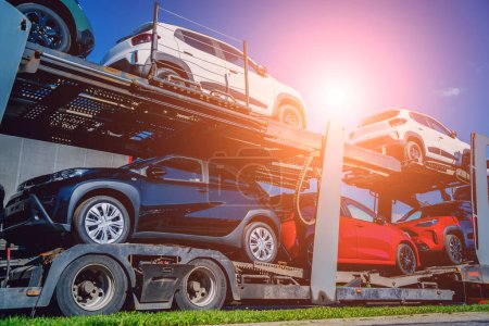 Car carrier trailer transports cars on highway at blue sky background