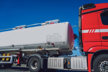 Téléchargez les photos : Camion citerne blanc transportant du carburant le long de la route sur le fond bleu ciel. - en image libre de droit