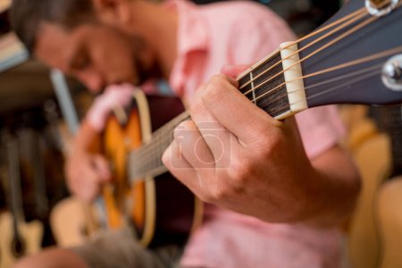 Téléchargez les photos : Jeune musicien testant la guitare classique dans un magasin de guitare. - en image libre de droit
