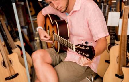 Téléchargez les photos : Jeune musicien accordant une guitare classique dans un magasin de guitare. - en image libre de droit