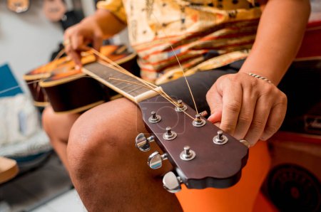Téléchargez les photos : Jeune musicien changeant de cordes sur une guitare classique dans un magasin de guitare. - en image libre de droit