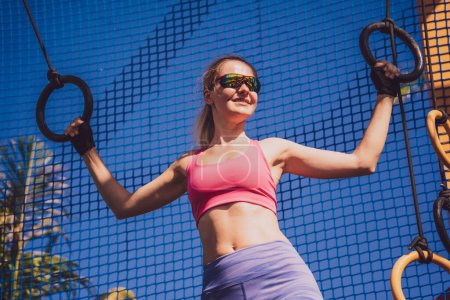 Photo for Athletic young woman exercising using gymnastic rings in a training camp. - Royalty Free Image
