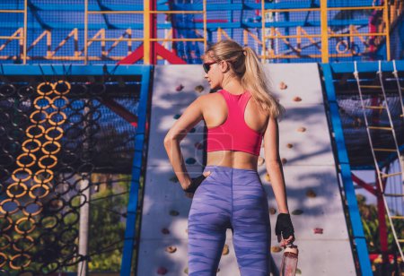 Téléchargez les photos : Jeune femme athlétique faisant de l'exercice et grimpant au rocher artificiel dans un camp d'entraînement - en image libre de droit
