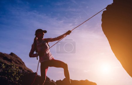 Photo for Young woman with a rope climbs to the top in the mountains near the ocean. - Royalty Free Image