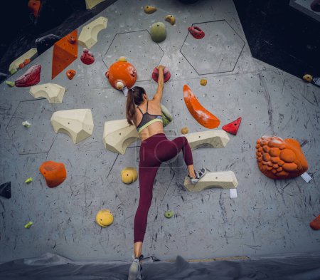Téléchargez les photos : Une grimpeuse forte escalade un mur artificiel avec des poignées et des cordes colorées - en image libre de droit