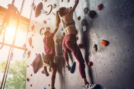 Téléchargez les photos : Un couple fort d'alpinistes escalade un mur artificiel avec des poignées et des cordes colorées - en image libre de droit
