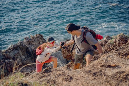Téléchargez les photos : Heureux jeune couple monte au sommet dans les montagnes près de l'océan. - en image libre de droit