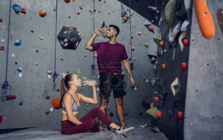 Téléchargez les photos : Un couple fort d'alpinistes se détendent près d'un mur artificiel avec des poignées et des cordes colorées - en image libre de droit