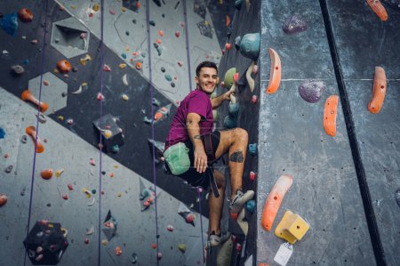 Foto de Un fuerte escalador macho trepa una pared artificial con pintorescos agarres y cuerdas - Imagen libre de derechos