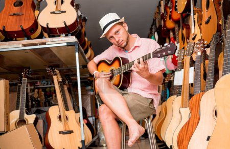 Téléchargez les photos : Jeune musicien testant la guitare classique dans un magasin de guitare. - en image libre de droit