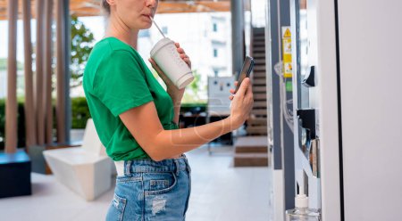 Foto de Mujer joven que paga por el café en la máquina expendedora utilizando el método de pago sin contacto. - Imagen libre de derechos