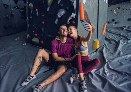 Photo for A strong couple of climbers against an artificial wall with colorful grips and ropes - Royalty Free Image